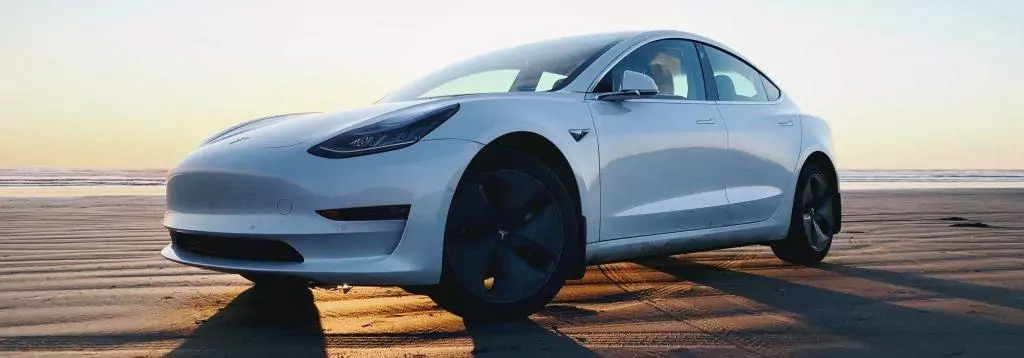 Tesla Model 3 with sun setting behind the car