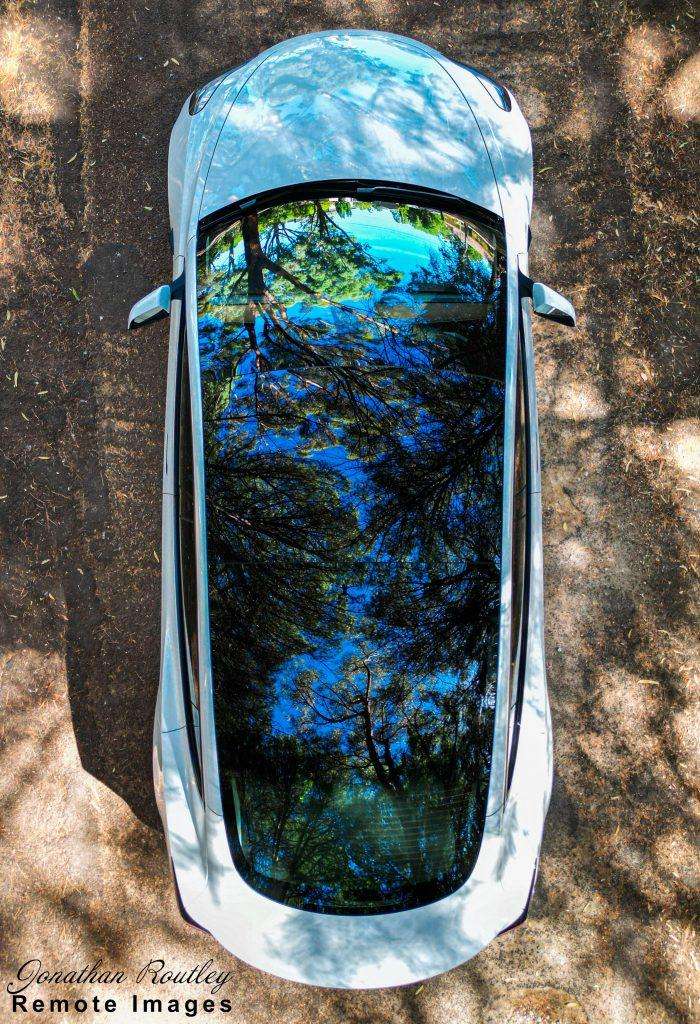 Tesla viewed from above with glass roof reflecting the surrounding trees.