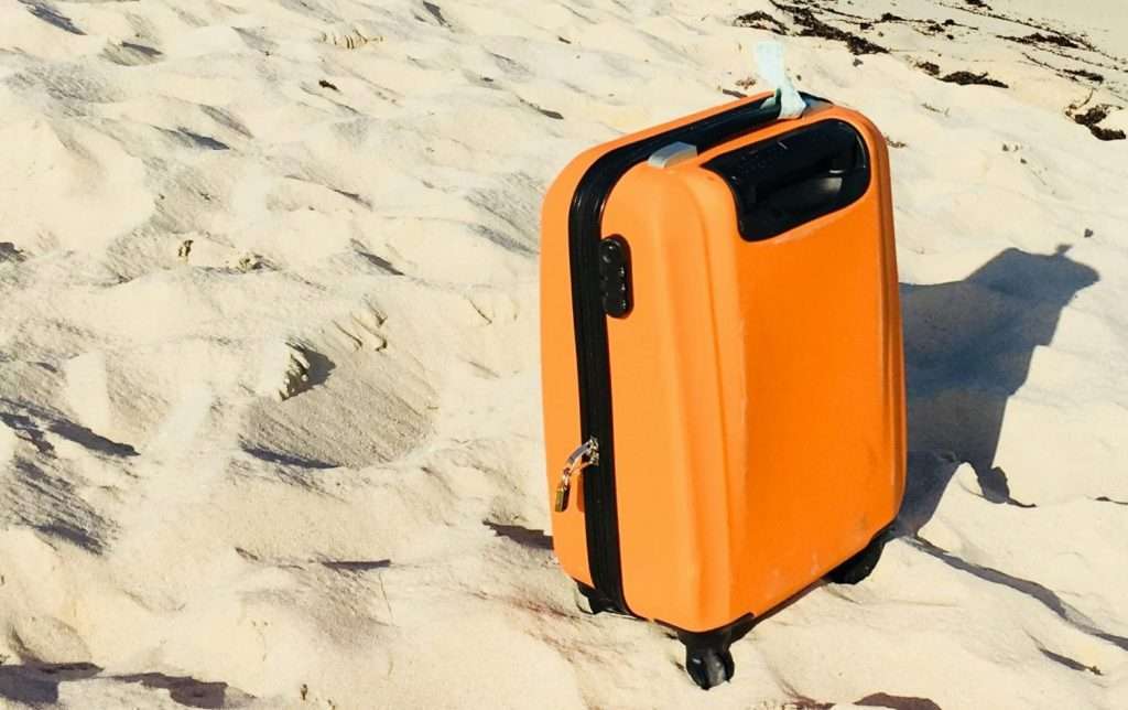 An orange suitcase closed standing up in the sand
