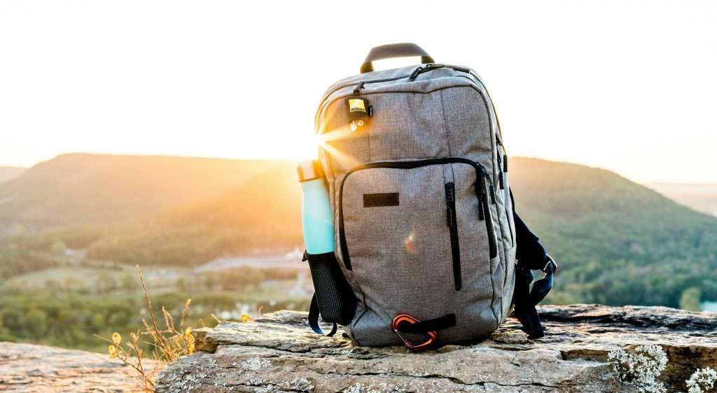 Backpack positioned standing up with blue water bottle and sunrise in background
