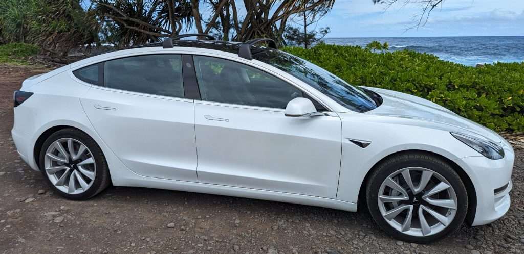 Model 3 along the Road to Hana in front of lush green vegetation and the ocean